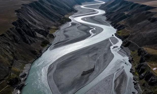 An aerial view of a braided river valley, silver channels splitting across gravel flats.