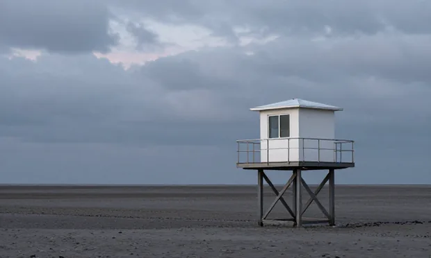A small weather station hut standing alone on a bleak grey shoreline at dusk.