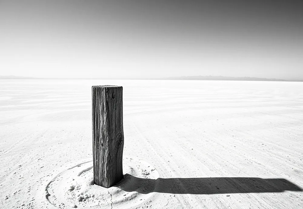Unattributed, Field Notation No. 7 — a high-contrast black and white photograph of a windswept salt flat with a single weathered survey stake.