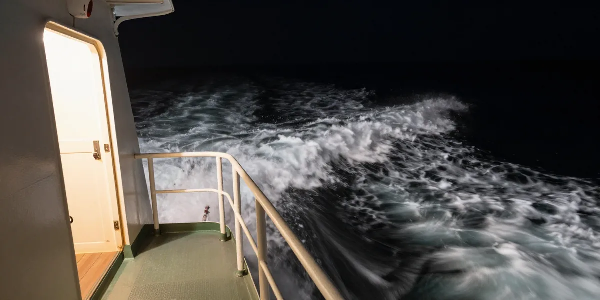 The white wake of a ship at night, lit by a rectangle of light from an open door