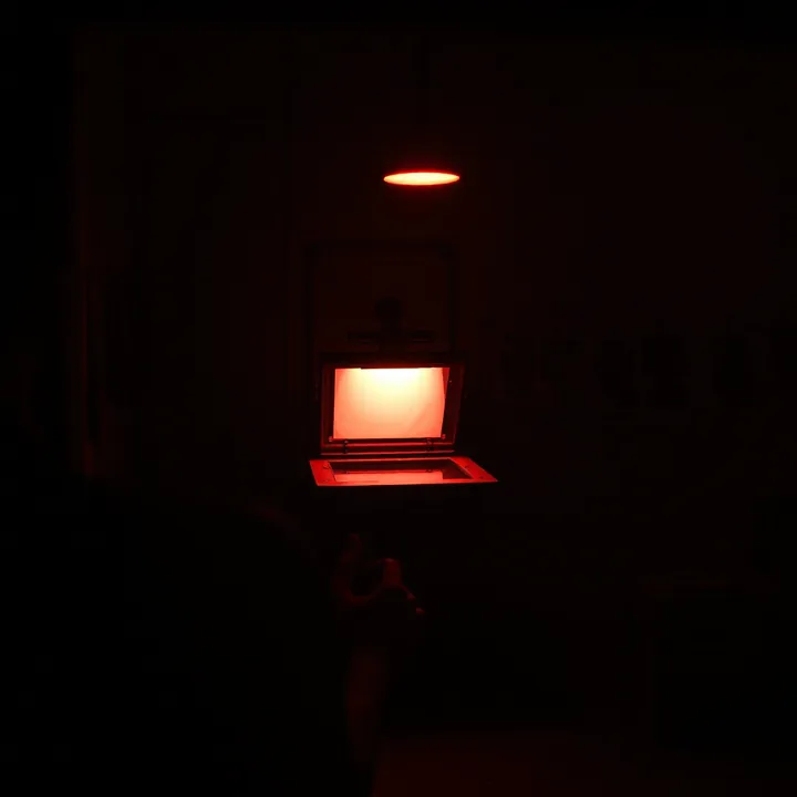 A figure turned away in the darkroom, lit only by the safelight