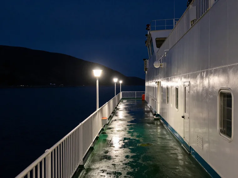 A night ferry deck arriving at a narrow northern sound, sodium lamps on wet steel railings