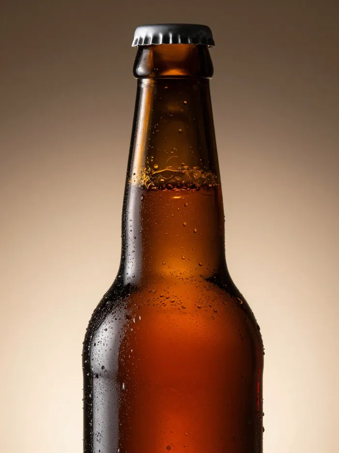 Dark amber bottle glass beaded with condensation in low warm light