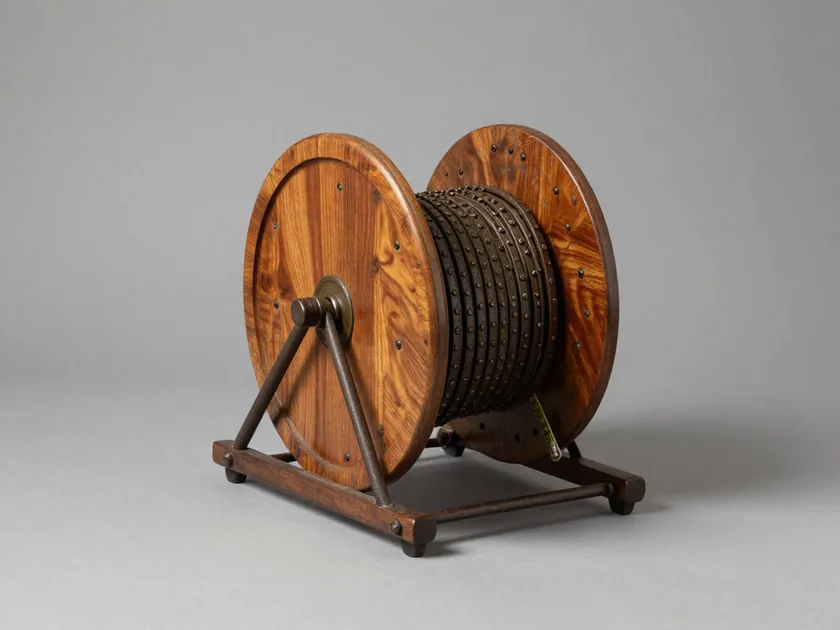 An elm surveyor's chain reel in its iron cradle, the wrought-iron measuring chain wound tight around the drum between two turned cheeks.