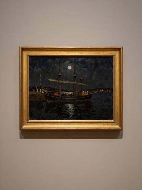 A dark oil nocturne of moored sailing brigs in a harbour under a low moon, in a plain gilt frame