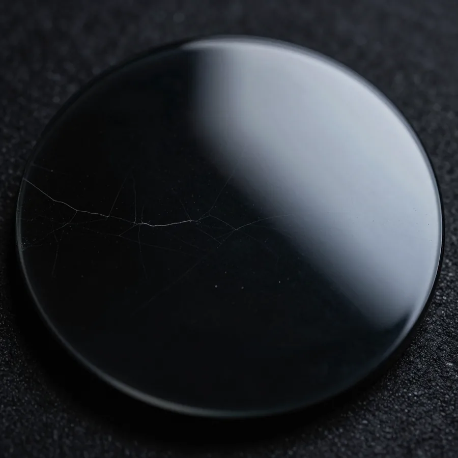 Macro of a polished black obsidian disc, faint conchoidal ripples under one grazing highlight