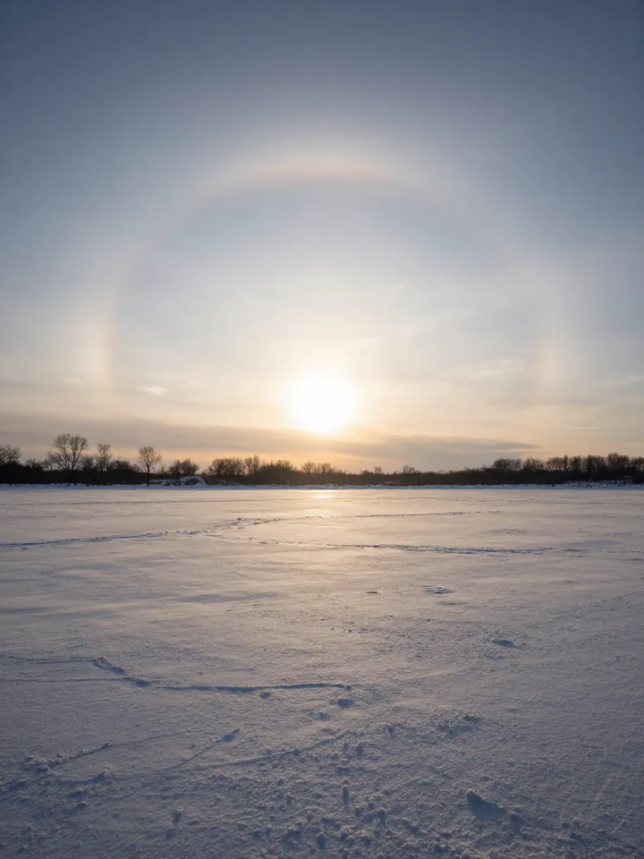 A low winter sun flanked by two bright sun dogs on a faint halo arc