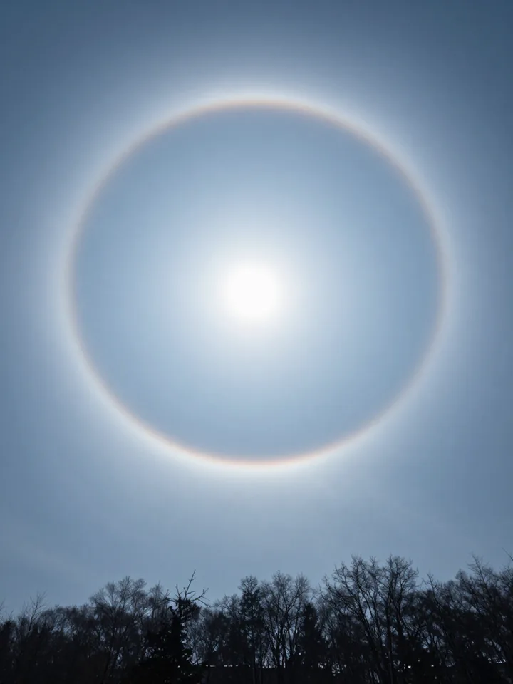 A pale twenty-two degree ring encircling a hazy sun in a blue sky