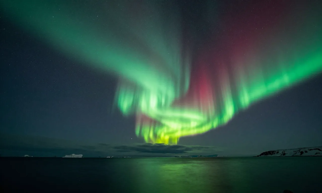 Green and rose aurora borealis folding over a dark arctic sea beneath a dense starfield