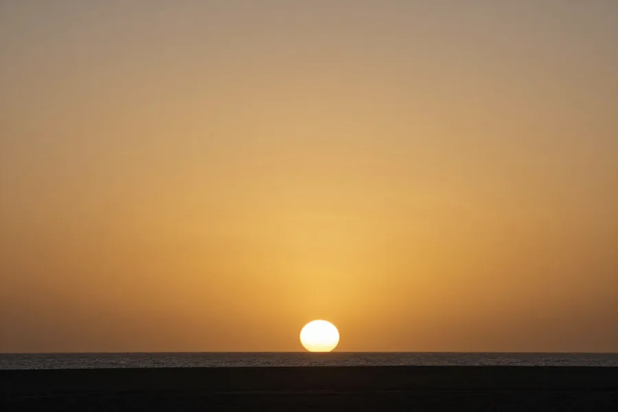 A low sun resting just above a flat sea horizon, the whole sky washed in level amber light.